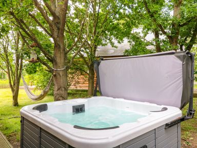An outdoor hot tub with water and an open cover near trees and a hammock at Dorado Lodge in Thorpe-on-the-Hill