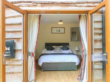 A bedroom with a double bed pillows bedside table lamp wall art and mirror at Dorado Lodge in Thorpe-on-the-Hill