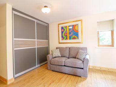 A room with a grey sofa two patterned cushions a framed colorful abstract painting wooden floor and grey sliding door closet at Dorado Lodge in Thorpe-on-the-Hill