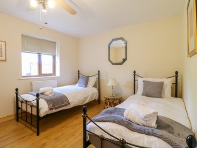 A bedroom with two single beds a small table with a lamp and a window at Dorado Lodge in Thorpe-on-the-Hill