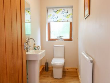 A bathroom with a toilet, pedestal sink, window with floral blind, wooden door and a radiator at Dorado Lodge in Thorpe-on-the-Hill