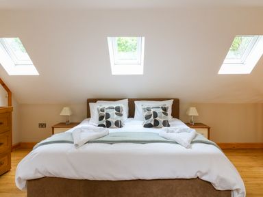 A bedroom with a bed a brown headboard two bedside tables with lamps three skylight windows and wooden flooring at Dorado Lodge in Thorpe-on-the-Hill