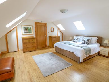 A bedroom with a large bed two wooden dressers a door two skylight windows and a rug on wooden floor at Dorado Lodge in Thorpe-on-the-Hill