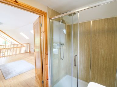 A bathroom with a glass shower enclosure next to a wooden door opening to a loft area with wooden flooring and skylights at Dorado Lodge in Thorpe-on-the-Hill
