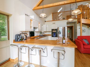 A kitchen with a wooden countertop and bar stools next to a red sofa at Dorado Lodge in Thorpe-on-the-Hill
