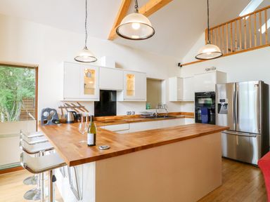 A kitchen with wooden countertops white cabinets stainless steel appliances and bar stools at Dorado Lodge in Thorpe-on-the-Hill