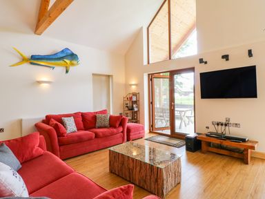 A living room with red sofas a mounted fish a wooden coffee table a wall mounted TV and glass doors at Dorado Lodge in Thorpe-on-the-Hill