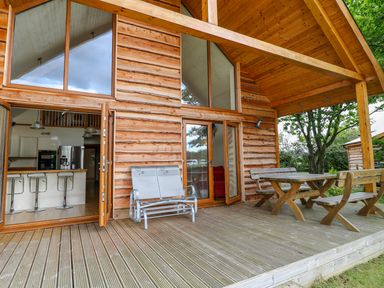 A wooden deck with metal and wooden outdoor furniture outside a log cabin with large windows at Dorado Lodge in Thorpe-on-the-Hill