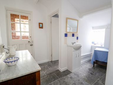 A hallway with a door leading outside a small sink with a mirror above and a table with a blue checkered tablecloth at Southrepps Lodge in Southrepps
