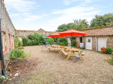 An outdoor courtyard with picnic tables and orange umbrellas surrounded by stone buildings at Southrepps Lodge in Southrepps