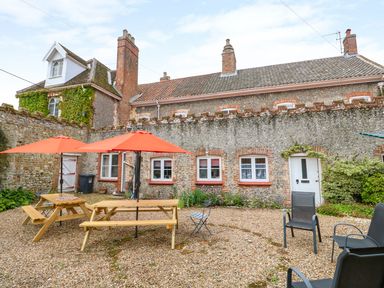 An outdoor gravel patio area with wooden picnic tables and orange umbrellas in front of a stone building with multiple windows and chimneys at Southrepps Lodge in Southrepps