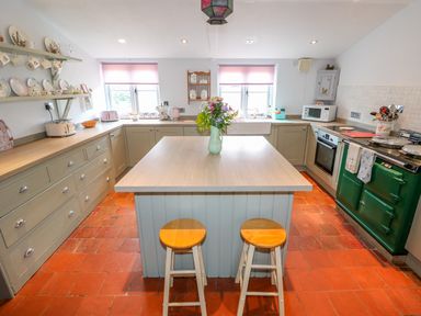 A kitchen with an island containing a vase of flowers and two stools and green cabinets with appliances at Southrepps Lodge in Southrepps