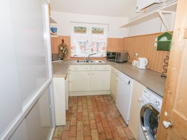 A narrow kitchen with white cabinets brick flooring a refrigerator washing machine and dishwasher at Southrepps Lodge in Southrepps