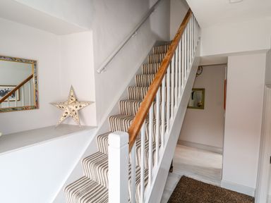 A staircase with striped carpet and wooden handrail beside a wall with a star decoration and a mirror at Southrepps Lodge in Southrepps