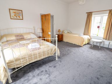 A bedroom with a double bed and a single bed a wooden door two nightstands and a window with striped curtains at Southrepps Lodge in Southrepps