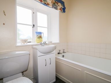 A bathroom with a toilet sink cabinet bathtub window and decorative jug at Southrepps Lodge in Southrepps
