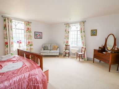 A bedroom with a wooden bed with pink bedding a loveseat two chairs a vanity with mirror and floral curtains at Southrepps Lodge in Southrepps
