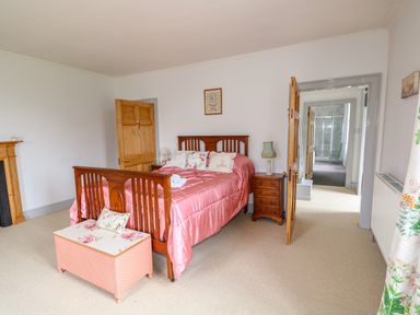 A bedroom with a wooden bed with pink bedding a wooden chest at the foot of the bed bedside tables with lamps an open door leading to a hallway at Southrepps Lodge in Southrepps