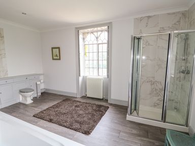 A bathroom with a shower enclosure a toilet a radiator under a window and a brown rug on the floor at Southrepps Lodge in Southrepps