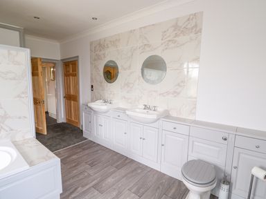 A bathroom with double sinks mirrors a toilet wooden doors and tiled walls at Southrepps Lodge in Southrepps