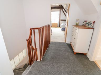 A hallway with grey carpet a wooden handrail a white chest of drawers and an open door showing a bedroom at Southrepps Lodge in Southrepps