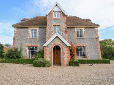 A two-story house with arched windows and a wooden door surrounded by gravel and bushes at Southrepps Lodge in Southrepps