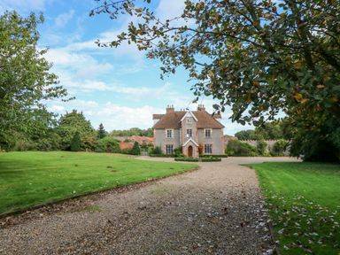 A large stone house at the end of a gravel driveway with lawn and trees around at Southrepps Lodge in Southrepps
