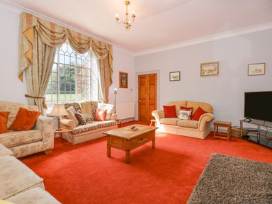 A living room with sofas a wooden coffee table a large window with curtains and a television at Southrepps Lodge in Southrepps