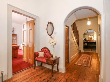 A hallway with wooden floor and an arched doorway showing stairs and a bench with a cushion and vase at Southrepps Lodge in Southrepps