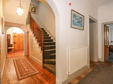 A hallway with wooden floor and carpet runner next to carpeted stairs and an open doorway in Southrepps Lodge Southrepps