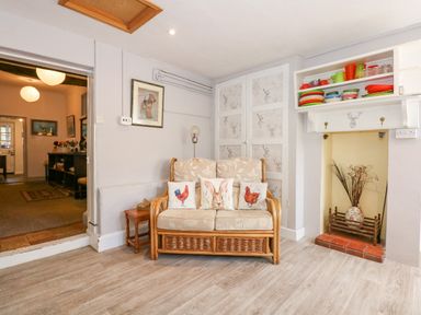 A small sitting area with a cushioned wicker loveseat and decorative pillows near a fireplace and shelving at Southrepps Lodge in Southrepps