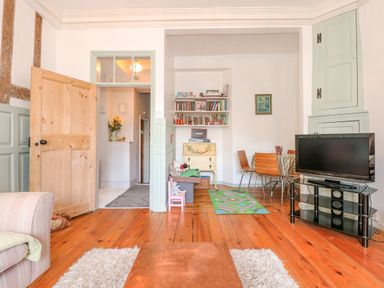 A living room with wooden floor a chair a television on a stand shelves with books and a table with chairs at Southrepps Lodge in Southrepps
