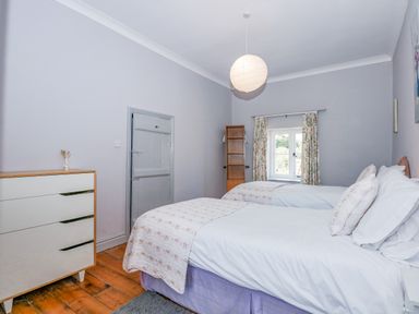 A bedroom with two single beds a wooden dresser and a window with floral curtains at Southrepps Lodge in Southrepps