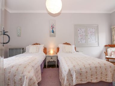 A bedroom with two single beds a nightstand between them a chair and a window at Southrepps Lodge in Southrepps