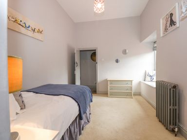 A bedroom with a bed a dresser a radiator a window seat with cushion and wall art at Southrepps Lodge in Southrepps