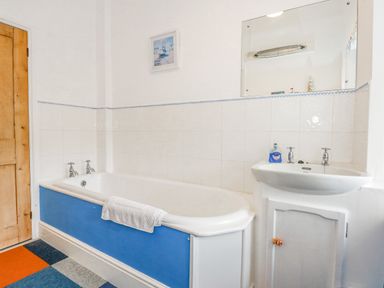 A bathroom with a blue panel bathtub a white sink with a blue soap bottle a wooden door and a mirror at Southrepps Lodge in Southrepps