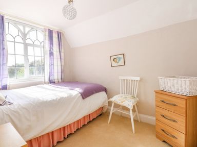 A bedroom with a single bed near a window a white chair next to a wooden chest of drawers with a basket on top at Southrepps Lodge in Southrepps