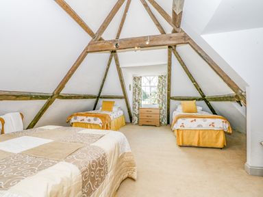 A bedroom with exposed wooden beams two single beds and a chest of drawers under a window at Southrepps Lodge in Southrepps