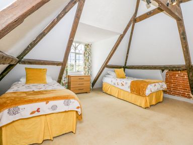 A bedroom with two single beds yellow bedding wooden beams a window and a chest of drawers at Southrepps Lodge in Southrepps