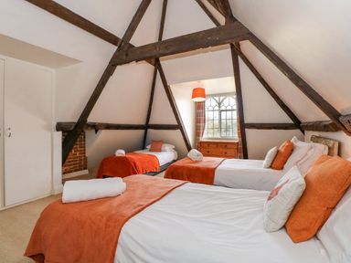 A bedroom with three beds orange blankets and pillows wooden beams and a window with a chest of drawers at Southrepps Lodge in Southrepps