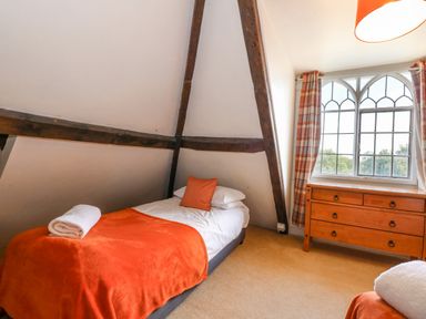 A bedroom with a single bed covered with an orange blanket and pillow a wooden dresser by a window with plaid curtains at Southrepps Lodge in Southrepps