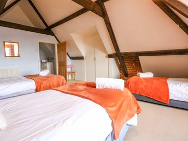 A bedroom with three single beds with orange blankets and rolled towels under a ceiling with exposed dark wooden beams at Southrepps Lodge in Southrepps