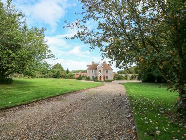 A gravel driveway leading to a two-story brick house with a lawn and trees on both sides at Southrepps Lodge in Southrepps
