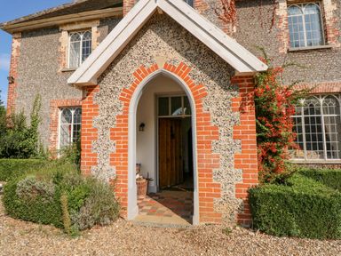 The entrance of a stone and brick house with arched doorway and plants surrounding it at Southrepps Lodge in Southrepps