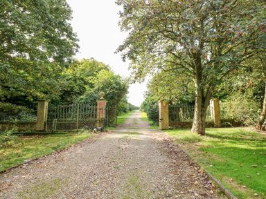 A gravel driveway leading through brick pillars and iron gates into a long tree-lined path at Southrepps Lodge in Southrepps