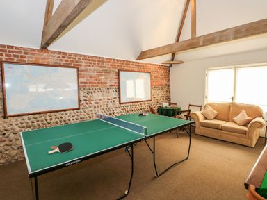 A game room with a ping pong table and paddles a sofa and framed maps on a brick and stone wall at Southrepps Lodge in Southrepps