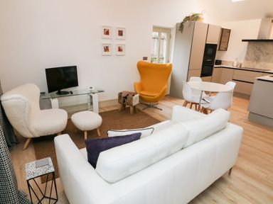 A living room with white and yellow chairs a glass TV stand and a round dining table at Sunshine Cottage in Preston under Scar near Leyburn