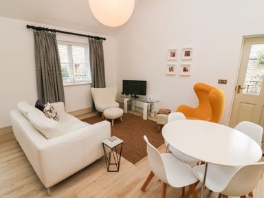 A living room with white sofa round dining table orange armchair and television at Sunshine Cottage Preston under Scar near Leyburn