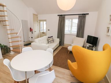 A living room with a white round dining table and chairs a yellow armchair a white sofa a beige armchair a spiral staircase and a small TV at Sunshine Cottage Preston under Scar near Leyburn
