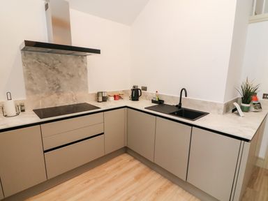 A kitchen with light brown cabinets black sink and faucet electric stove and kettle at Sunshine Cottage Preston under Scar near Leyburn